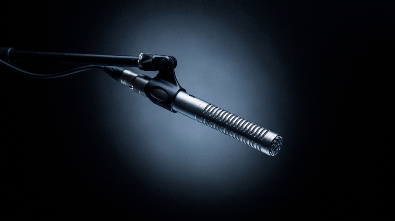 Shotgun microphone on a boom mount in studio light.